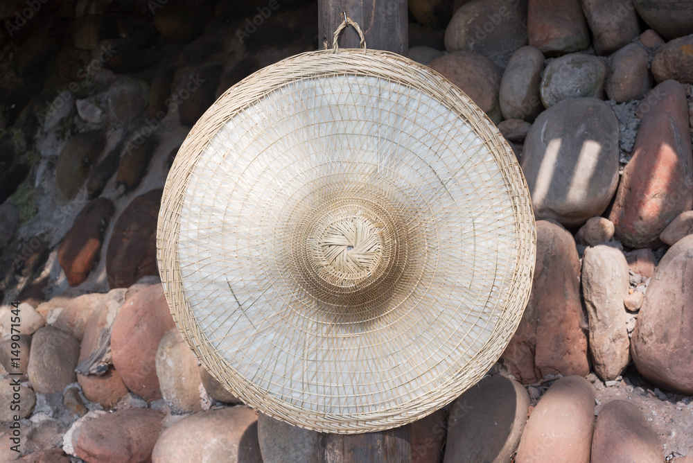 Chinese straw hat hanging on a stone wall in the countryside - C