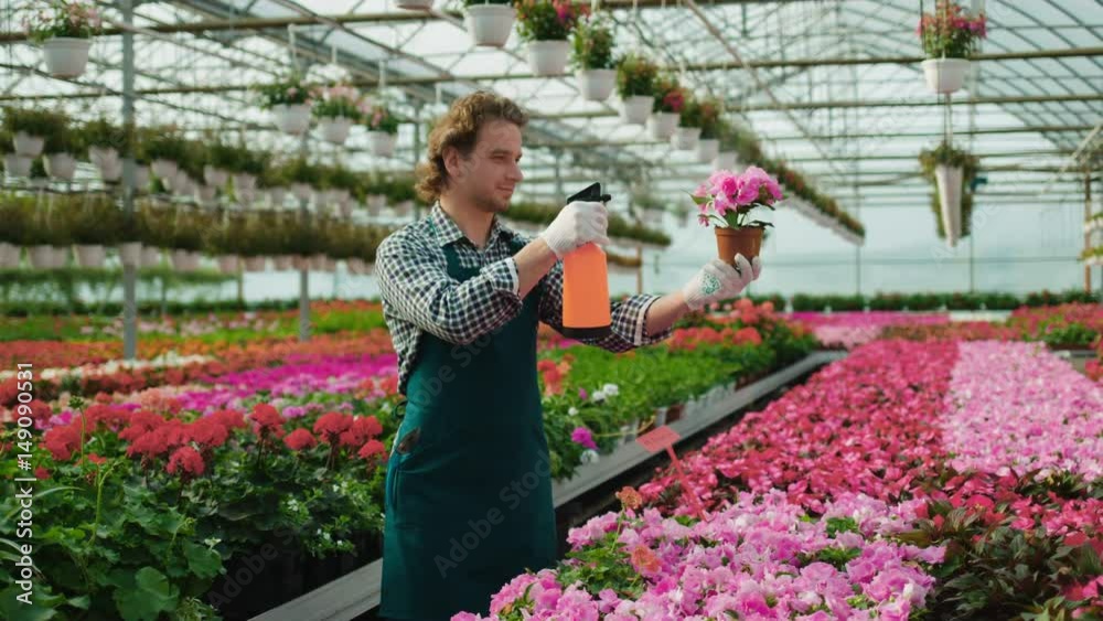 Attractive man florist is sprinkling flowers with water. Man is standing at garden center and smiling. Attractive man florist is sprinkling flowers with water. Man is standing at garden center and smiling.