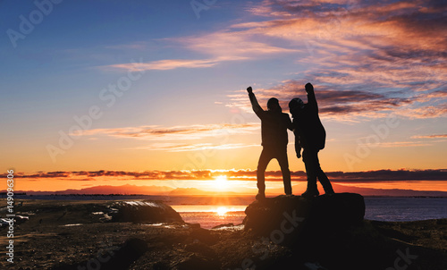 Silhouette two man success achievement goals  rise hand up on peak mountain  in morning sunrise