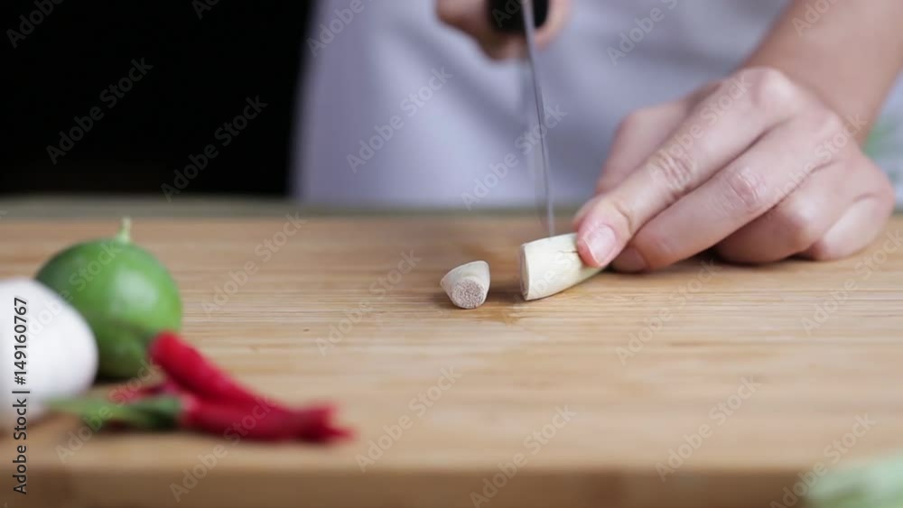 A female hand slicing lemongrass on bamboo wooden plate with other Thai herbs beside. A female hand slicing lemongrass on bamboo wooden plate with other Thai herbs beside.