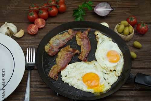 Fried eggs and bacon in a pan for breakfast on a wooden background
