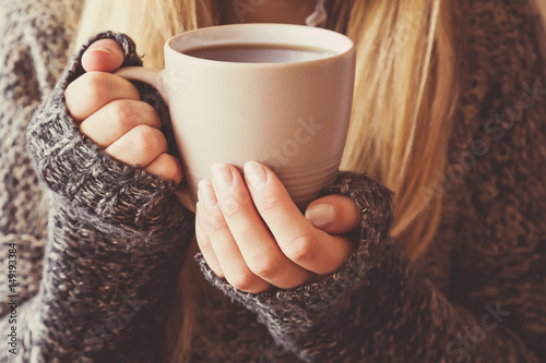 Canvas Print Young woman's hands holding a mug and warming with hot coffee.