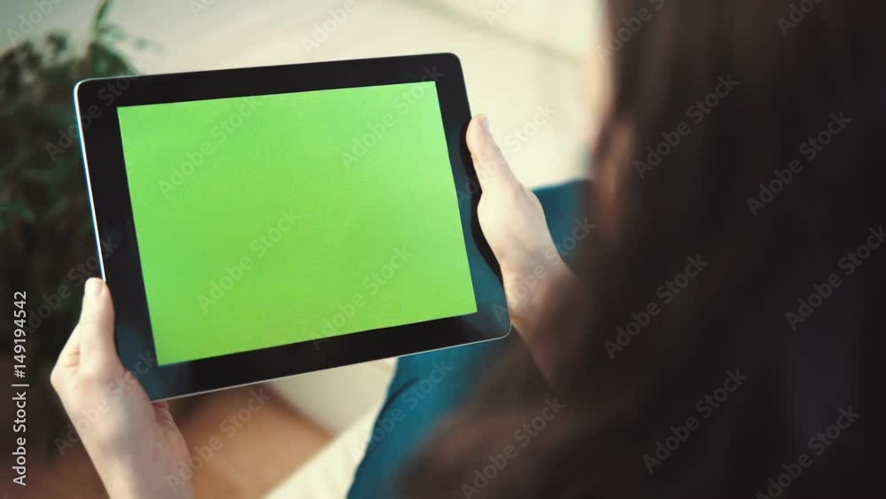 Indoor shot of a woman using tablet pc with green screen sitting on white sofa, pick and slide gestures, horizontal orientation