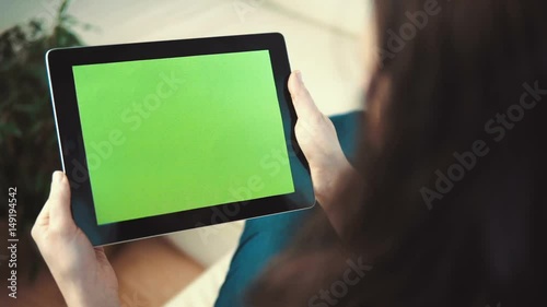 Indoor shot of a woman using tablet pc with green screen sitting on white sofa, pick and slide gestures, horizontal orientation