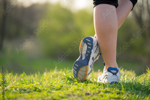 Young girl feet in sport shoes sneakers on green grass on meadow in spring. Lifestyle and fitness