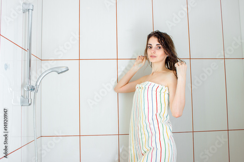 girl standing in a bathtub in a large towel and straightens hair photo