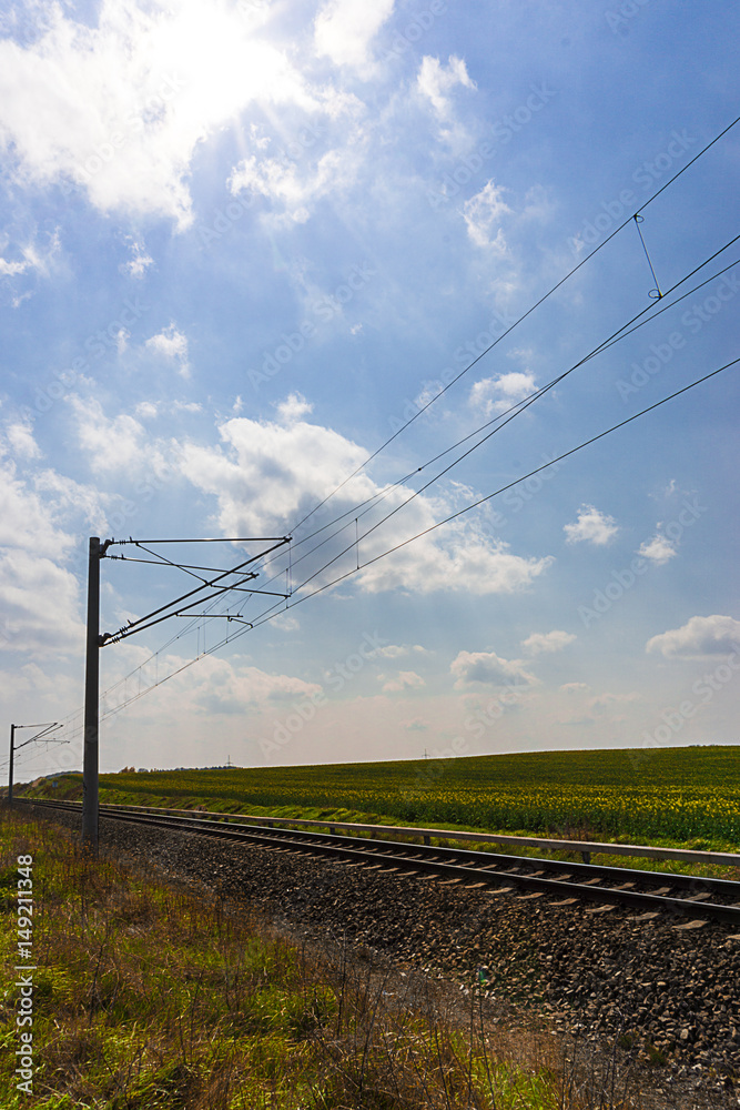 Eisenbahnlinie mit Oberleitung vor einem rapsfeld