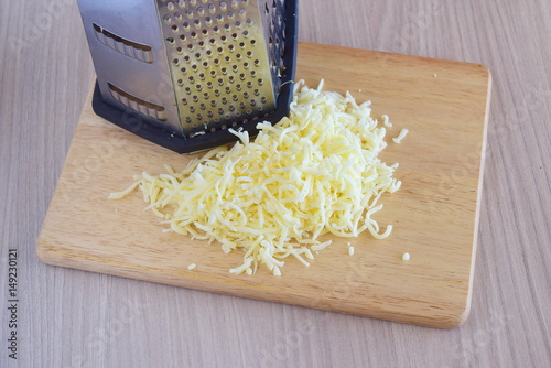 Step by step cooking. Grated mozarella cheese with a grater on a wooden cutting board on a grey background