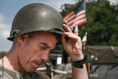Tired Vietnam War era soldier puts oh his helmet, with American flag in background