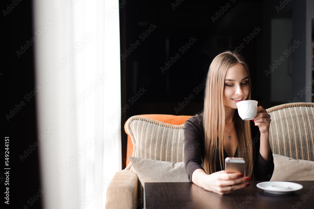 Young woman drinking coffee in a cafe and using a mobile phone Young woman drinking coffee in a cafe and using a mobile phone