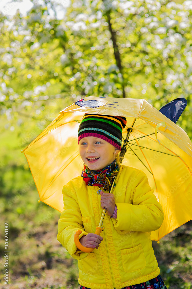 Portrait  cute little girl with yellow umbrella and yellow jacket on sunny spring day in the park