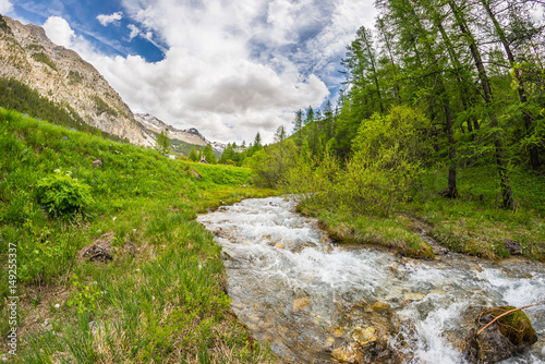 Flowing transparent waters on high altitude alpine stream in idyllic uncontaminated environment in the Italian French Alps. Ultra wide angle view.