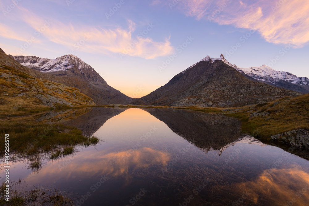 High altitude alpine lake in idyllic land with reflection of majestic rocky mountain peaks glowing at sunset. Wide angle view on the Alps.