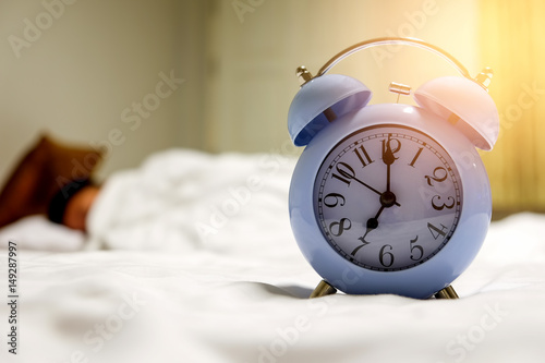 Alarm clock set at 7:00 am with people sleep blurred background.