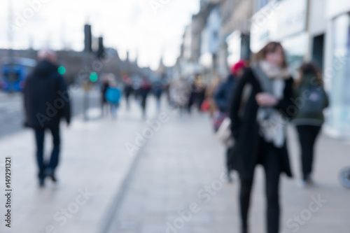 Blurred image of People walking on the street, with car, building in background. On Princes Street, the main shopping street in Edinburgh, United Kingdom.