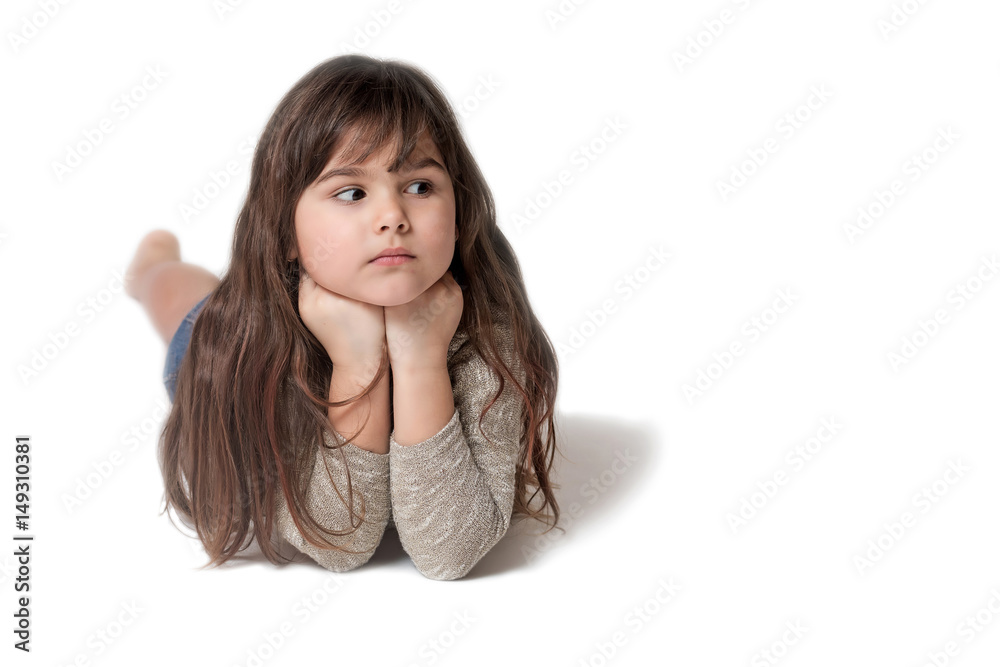 Brunette long haired little girl is lying on the gray background. The girl is supporting her chin with both hands and is looking at the empty place of the photo ready for your text. Brunette long haired little girl is lying on the gray background. The girl is supporting her chin with both hands and is looking at the empty place of the photo ready for your text.