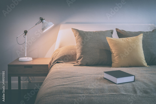 vintage style photo of cozy bedroom interior with book and reading lamp on bedside table photo