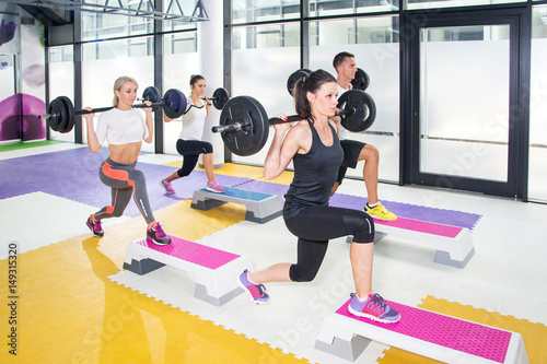 Group of sporty people lifting barbells over their heads at a gym.