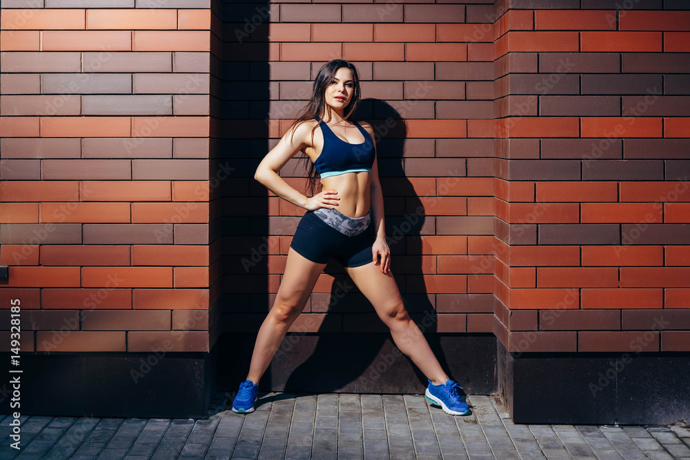 Attractive young woman in sportswear posing against a brick wall background with copyspace. Training outdoors.