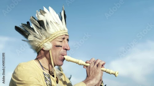 An Indian in a national costume plays a flute on the river bank 4k
