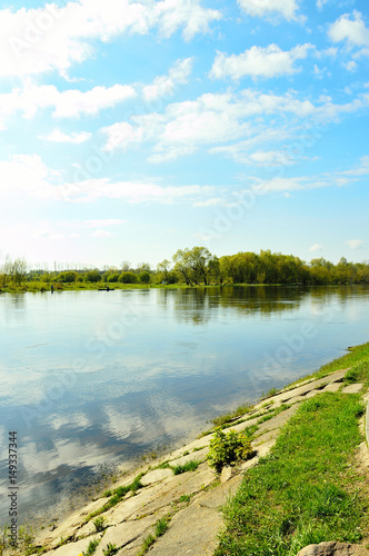 Fototapeta Naklejka Na Ścianę i Meble -  Rzeka i brzeg z trawą z niebem z chmurami.