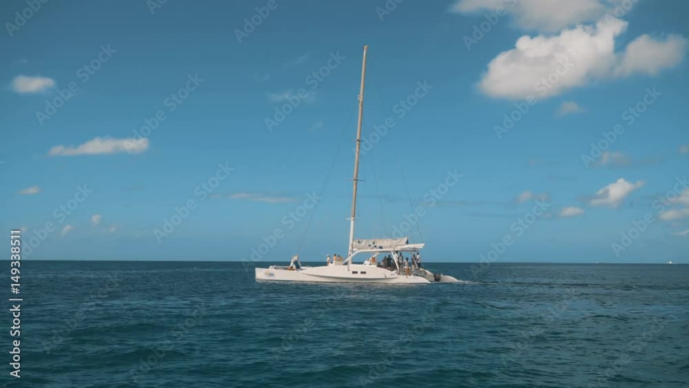 Big luxury cataman sailboat catamaran on the horizon in the beautiful Caribbean sea shooting from other boat on the movie midday sunny. Teal and orange 4k ultra hd style. Blue sky with little clouds Big luxury cataman sailboat catamaran on the horizon in the beautiful Caribbean sea shooting from other boat on the movie midday sunny. Teal and orange 4k ultra hd style. Blue sky with little clouds