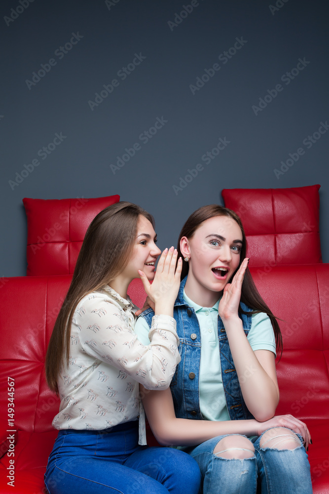 Two pretty girls gossiping on red leather couch Two pretty girls gossiping on red leather couch