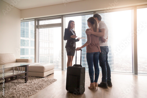 Female real estate agent showing property to young interested couple travellers, just arrived with baggage, tenants moving in or out rented apartment, renting flat on trip, daily rent abroad
