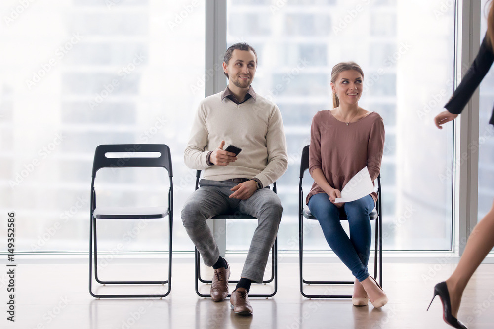 Confident businesswoman walking by male and female job candidates sitting on chairs, following her with their eyes, fake artificial smile, pretending amiability, mask of pretense, social artifice Confident businesswoman walking by male and female job candidates sitting on chairs, following her with their eyes, fake artificial smile, pretending amiability, mask of pretense, social artifice