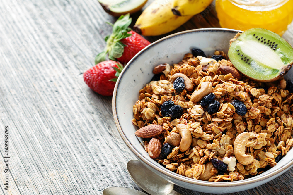 Fototapeta premium Healthy breakfast food: bowl of muesli granola, fruits and honey on wooden table. Closeup view, copy space
