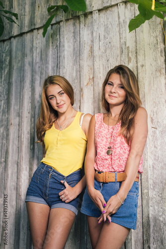Two happy teenage girls friends wearing Tshirts and jeans shorts smiling over pale wooden background © stormy