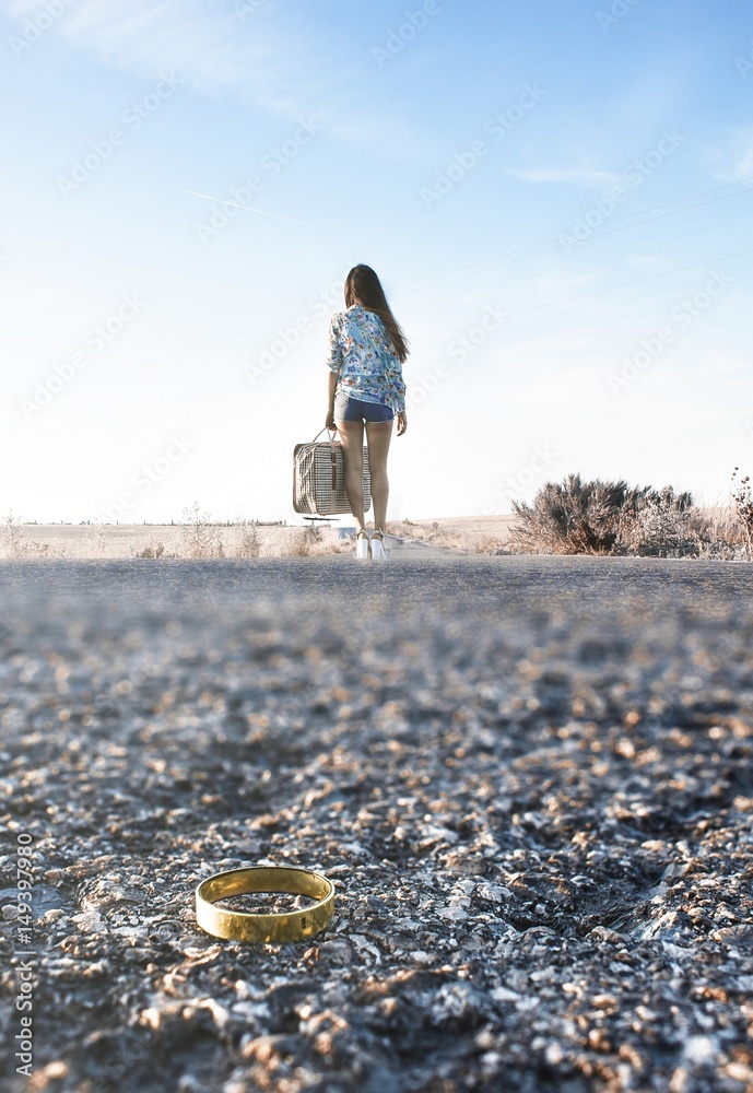 Fototapeta premium Chica recién divorciada de espaldas con maleta de viaje andando por la carretera.