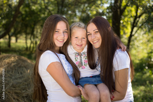 Three happy sisters hugging and smiling joyfully in summer park