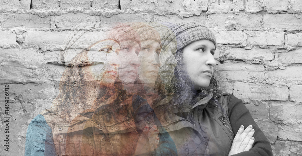 Multiple exposures of young woman standing with crossed arms against urban wall looking away