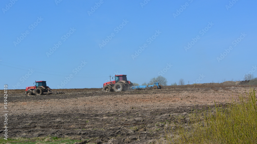 Two red tractors cultivate the field, agriculture, spring landscape, outskirts 
