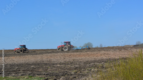 Two red tractors cultivate the field  agriculture  spring landscape  outskirts 