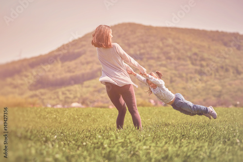 Mother and daughter playing circling around outdoors on a green field. Mother and little girl enjoying time together. Happy family concept