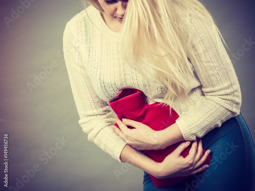 Woman feeling stomach cramps holding hot water bottle
