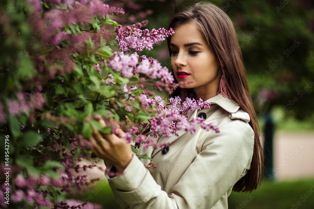 beautiful young woman in a trench coat near blooming lilac beautiful young woman in a trench coat near blooming lilac