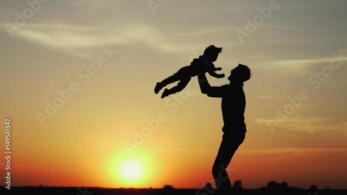 Happy child rushes into hands of father. Family hugs over sunset sky background. Silhouettes of anonymous boy and man outside in summer or autumn landscape. Slow motion 180fps