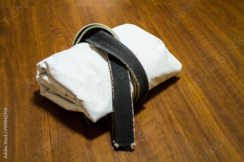 Black belt and Gi for martial arts ( Karate, Judo, Jiu-Jitsu, Kenpo, Taekwondo, Budo) on the wood floor