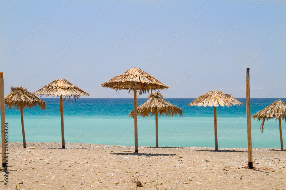Straw parasols on a beach, in the background a turquoise sea
