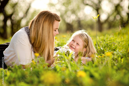 Mother with daughter a little blond girl  lying in the garden or park on the grass with flowers  love  family  communication