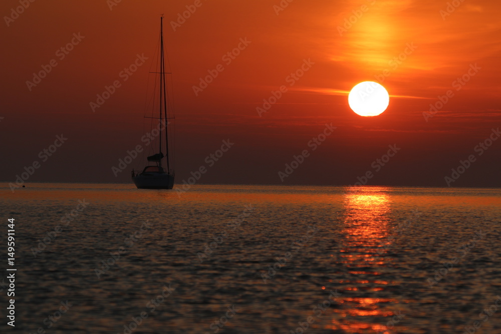 Segelboot ankert vor der Küste bei romantischem Sonnenaufgang Segelboot ankert vor der Küste bei romantischem Sonnenaufgang