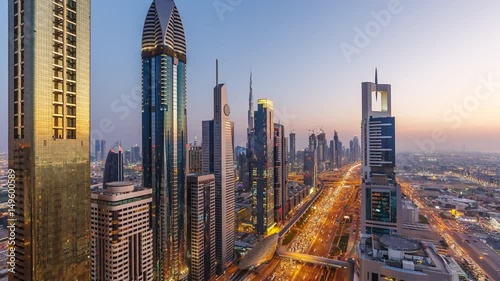 Downtown Dubai skyscrapers at sunset. Scenic aerial view of famous highway with fast moving traffic. 4K day-to-night transition time lapse.