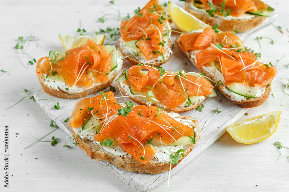 Smoked salmon bruschettas with soft cheese and cucumber shavings on white board.