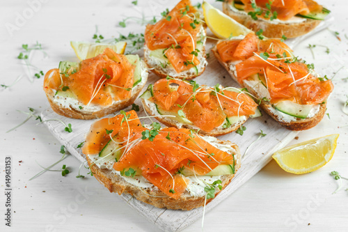 Bild auf Leinwand Smoked salmon bruschettas with soft cheese and cucumber shavings on white board