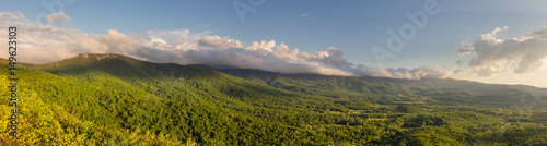 Panorama of the Shenandoah Valley at golden hour as seen from Shenandoah National Park with the forest a bright  vibrant green and clouds in the sky