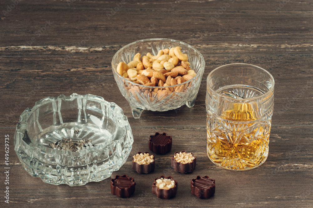 Glass of whiskey, a cuban cigar, nuts and chocolates on a grey wooden table. Close-up view. Glass of whiskey, a cuban cigar, nuts and chocolates on a grey wooden table. Close-up view.