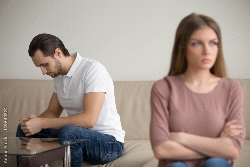 Upset depressed guy sitting on couch deep in thoughts, frustrated couple after quarrelling, guilty man regretting about mistake thinking of resolving conflict, offended woman not going to forgive Upset depressed guy sitting on couch deep in thoughts, frustrated couple after quarrelling, guilty man regretting about mistake thinking of resolving conflict, offended woman not going to forgive
